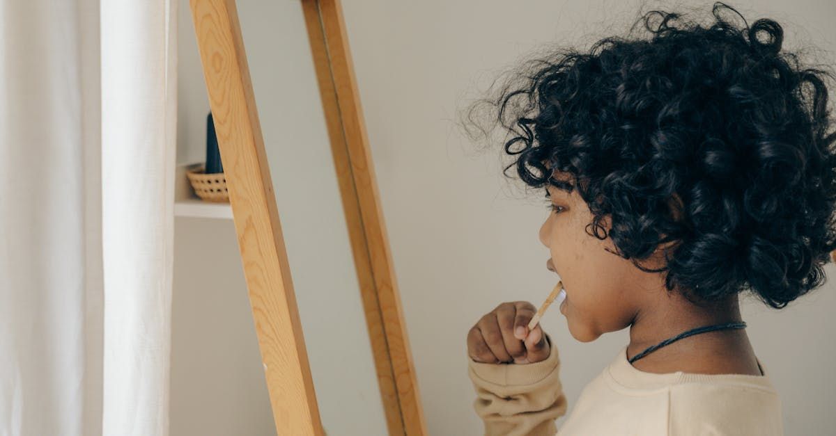 little kid brushing teeth while looking in the mirror