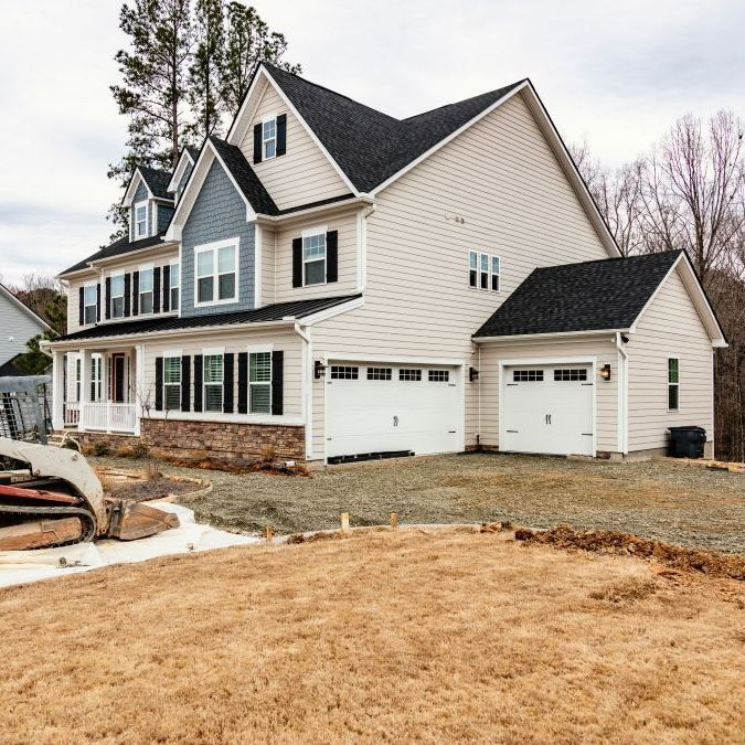 A large house is under construction with a bulldozer in front of it