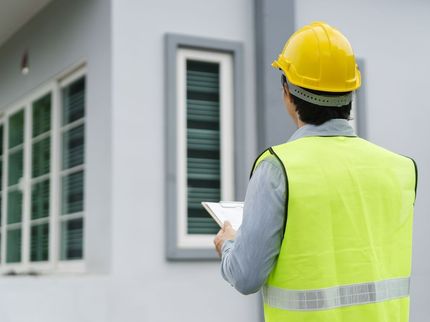 A construction worker wearing a hard hat and safety vest is looking at a tablet.