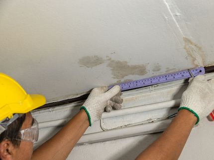 A man wearing a hard hat and gloves is measuring a pipe with a ruler.