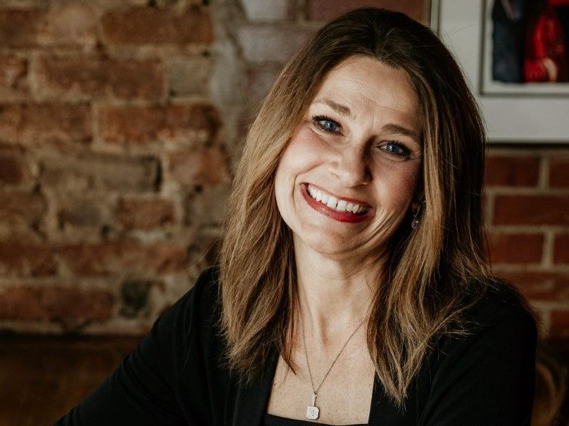 A woman is smiling in front of a brick wall.