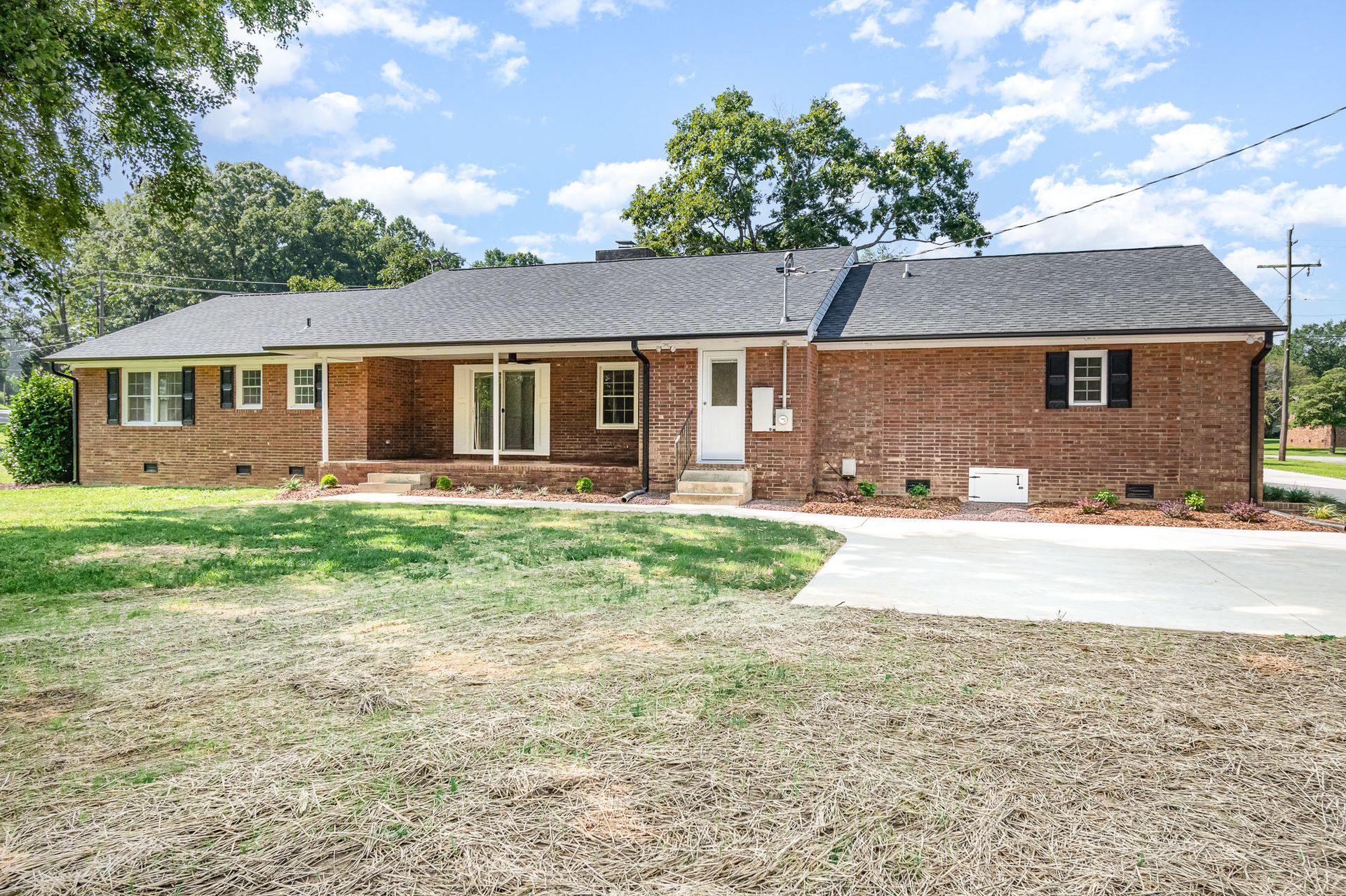 Brick ranch house with a green yard, driveway, and blue sky.