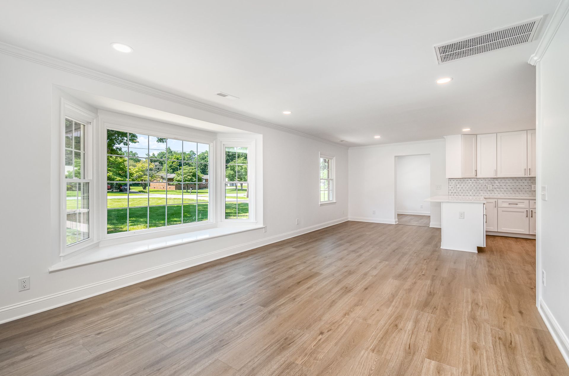 Empty living room with a bay window, hardwood floor, and white walls.