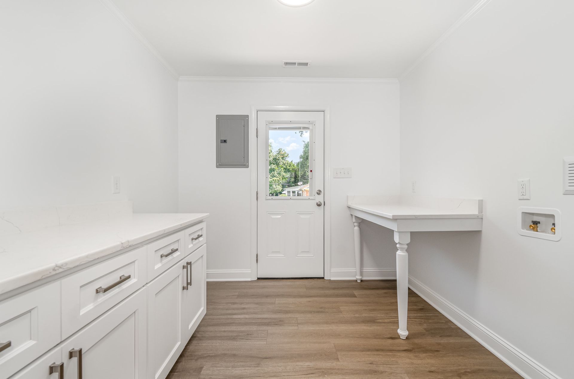 White laundry room with cabinetry, a small table, and a door to the outside.