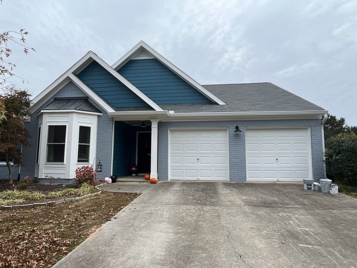 A blue house with white garage doors that had siding replaced and painted