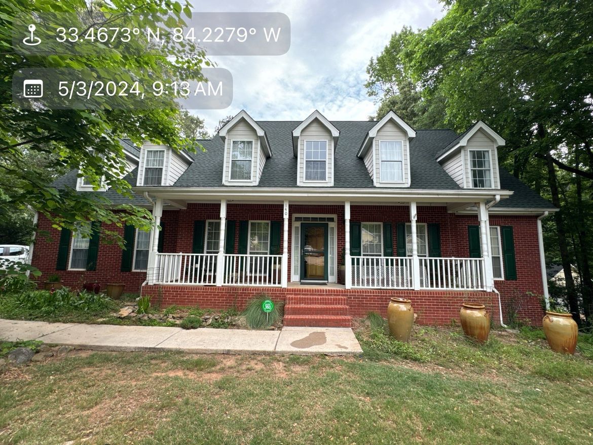 A large red brick house with a large porch and a black roof.