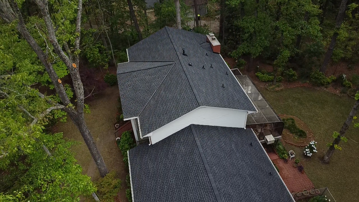 An aerial view of a house with a roof that is surrounded by trees.