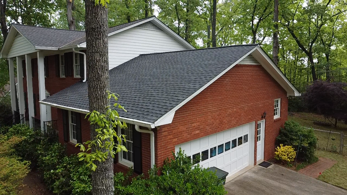 An aerial view of a brick house with a garage and trees in the background.