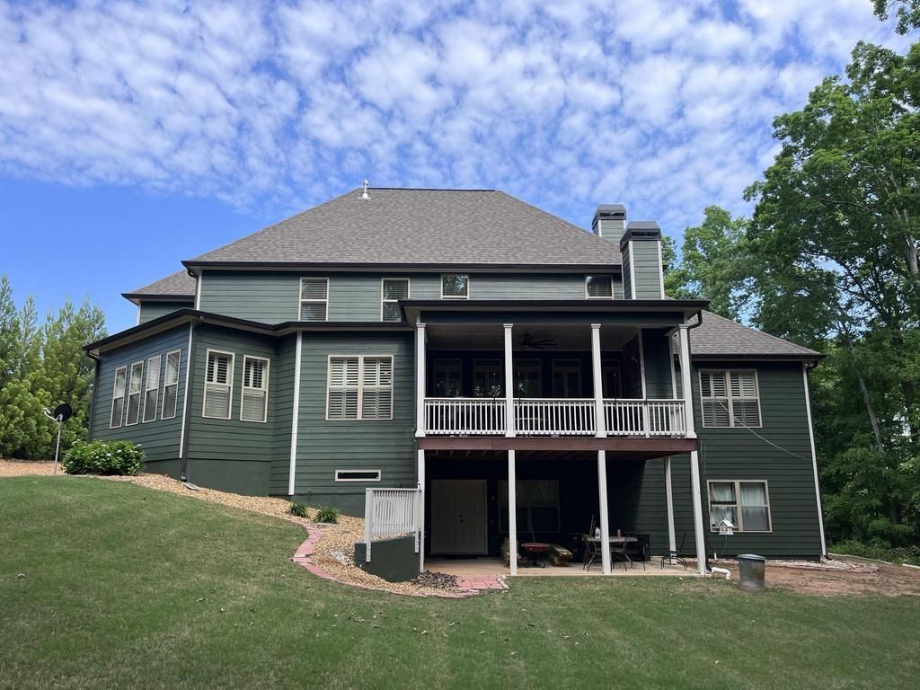 The back of a large green house with a large porch.