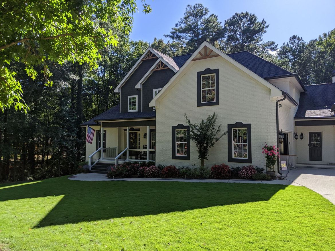 A large white house with a black roof is surrounded by trees