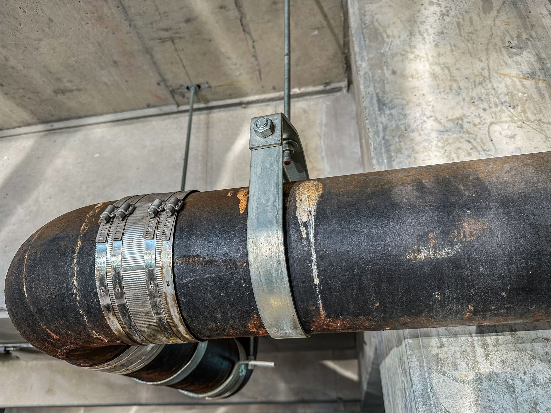 Rusty insulated pipe secured to a concrete ceiling with metal straps