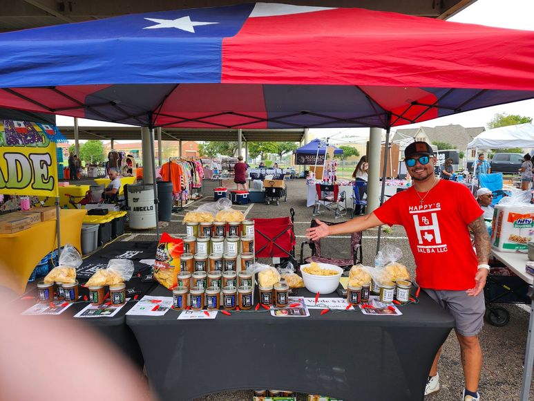 A man in a red shirt is standing in front of a table at a market.