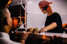 A woman is serving hamburgers to a man at a food truck.