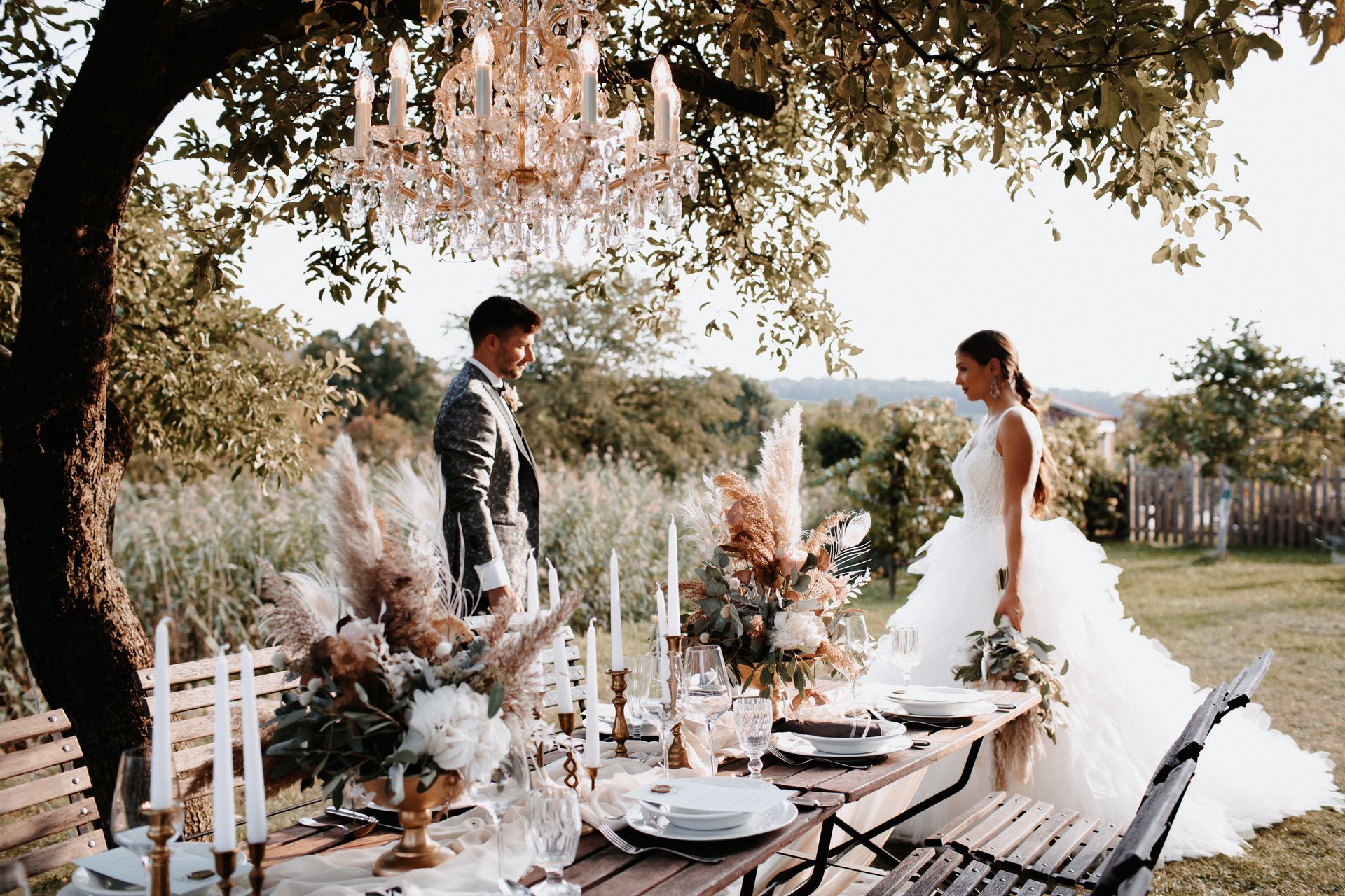 Gedeckter Tisch im Garten für Hochzeitsessen mit Brautpaar im Hintergrund.