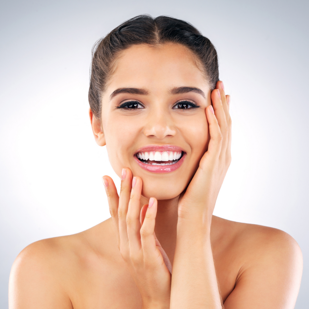 Smiling person with clear skin touching their face with both hands against a plain light background.
