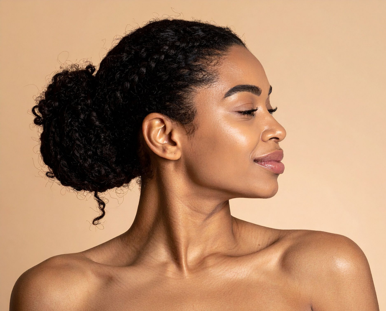 A person with hair styled in a back bun, shown in profile against a tan background with a soft, neutral expression.