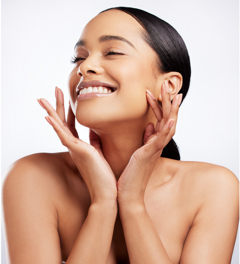 A smiling person with hands gently touching their cheeks against a plain white background.