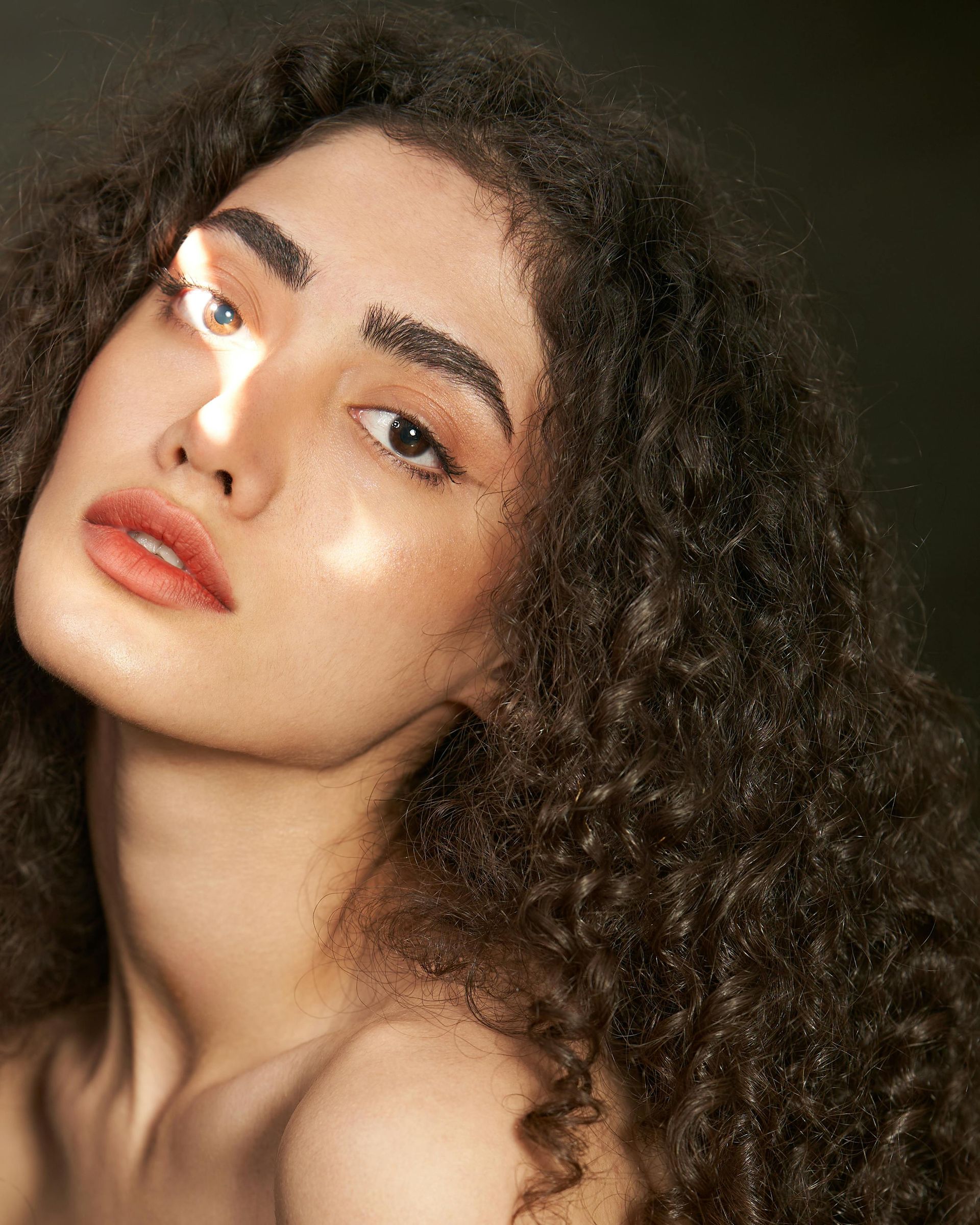 A close-up portrait of a person with curly dark hair, freckles, and light makeup.