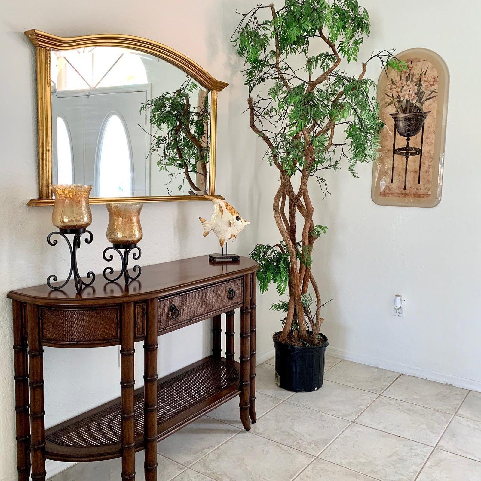 A hallway with a wooden console table, a large mirror, decor, and a potted tree.