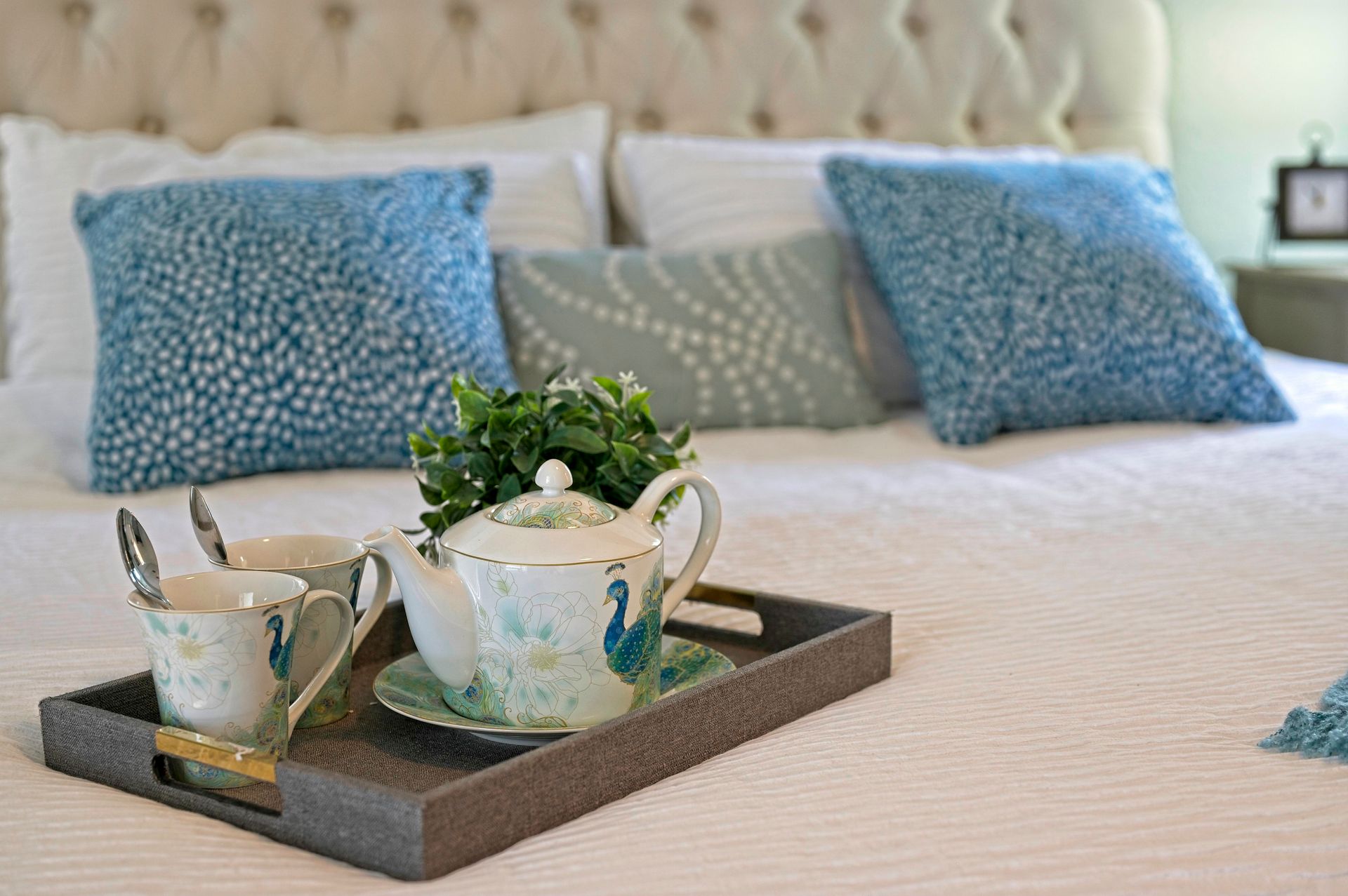 Bed with tray set for tea; teapot, cups, and pillows in shades of blue and white.