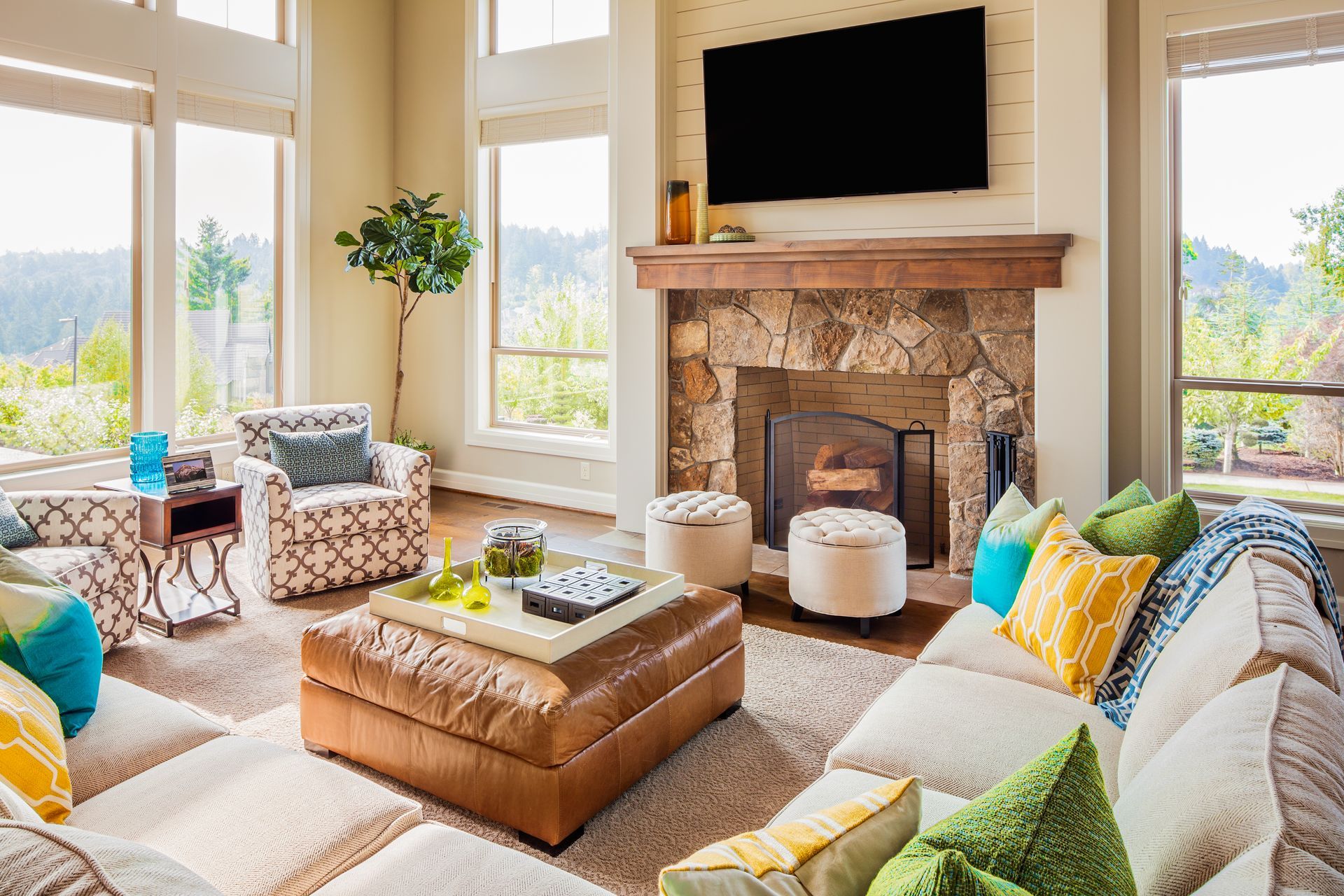 Cozy living room with fireplace, large windows, sectional sofa, and brown leather ottoman.