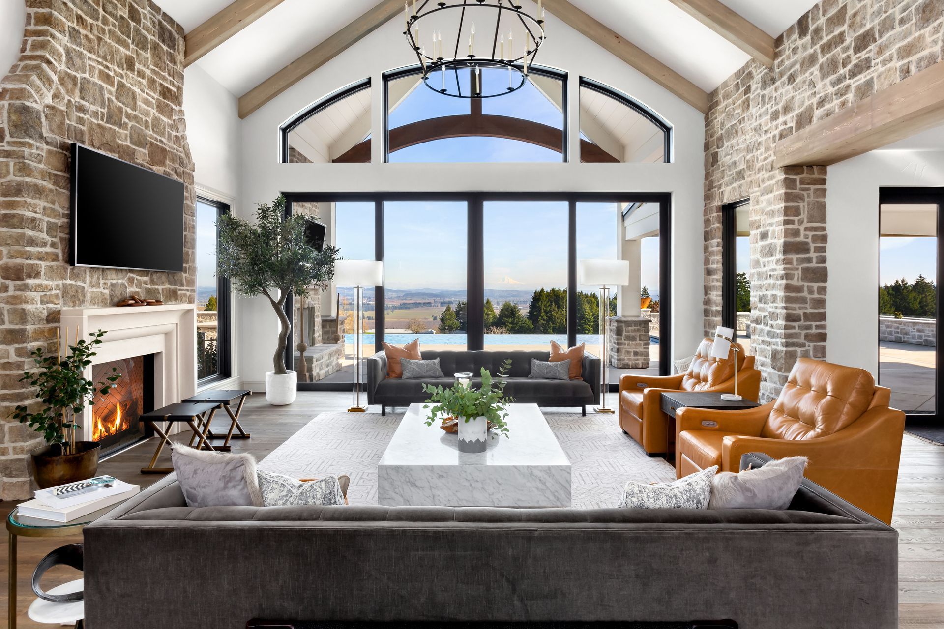 Luxurious living room with stone walls, fireplace, and panoramic windows overlooking a scenic view.