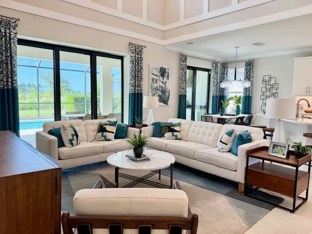 Living room with white sofas, teal accents, large windows, and a round coffee table.