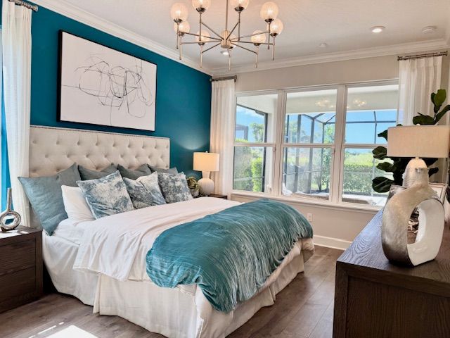 Bedroom with teal accent wall, bed, nightstands, and windows.