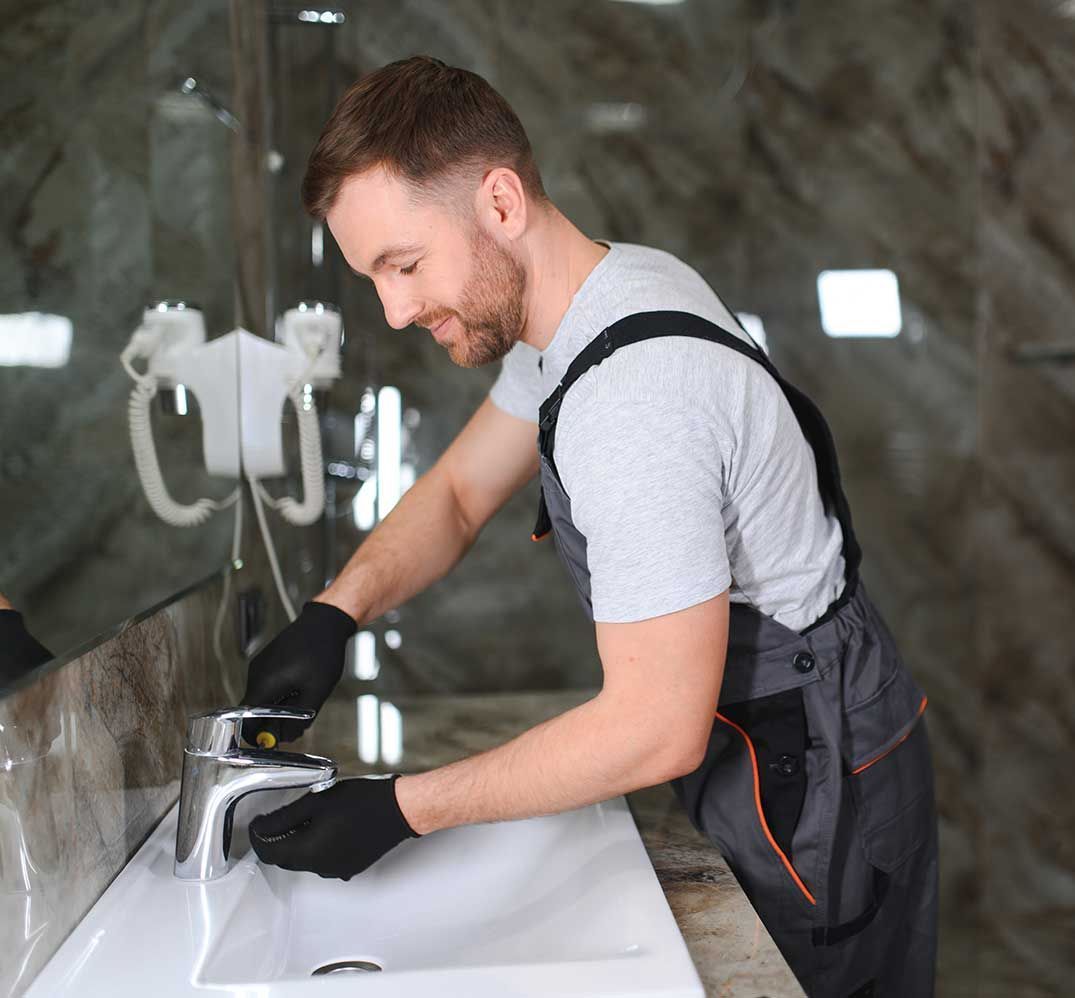 En mand er ved at ordne en vandhane i en badeværelsesvask