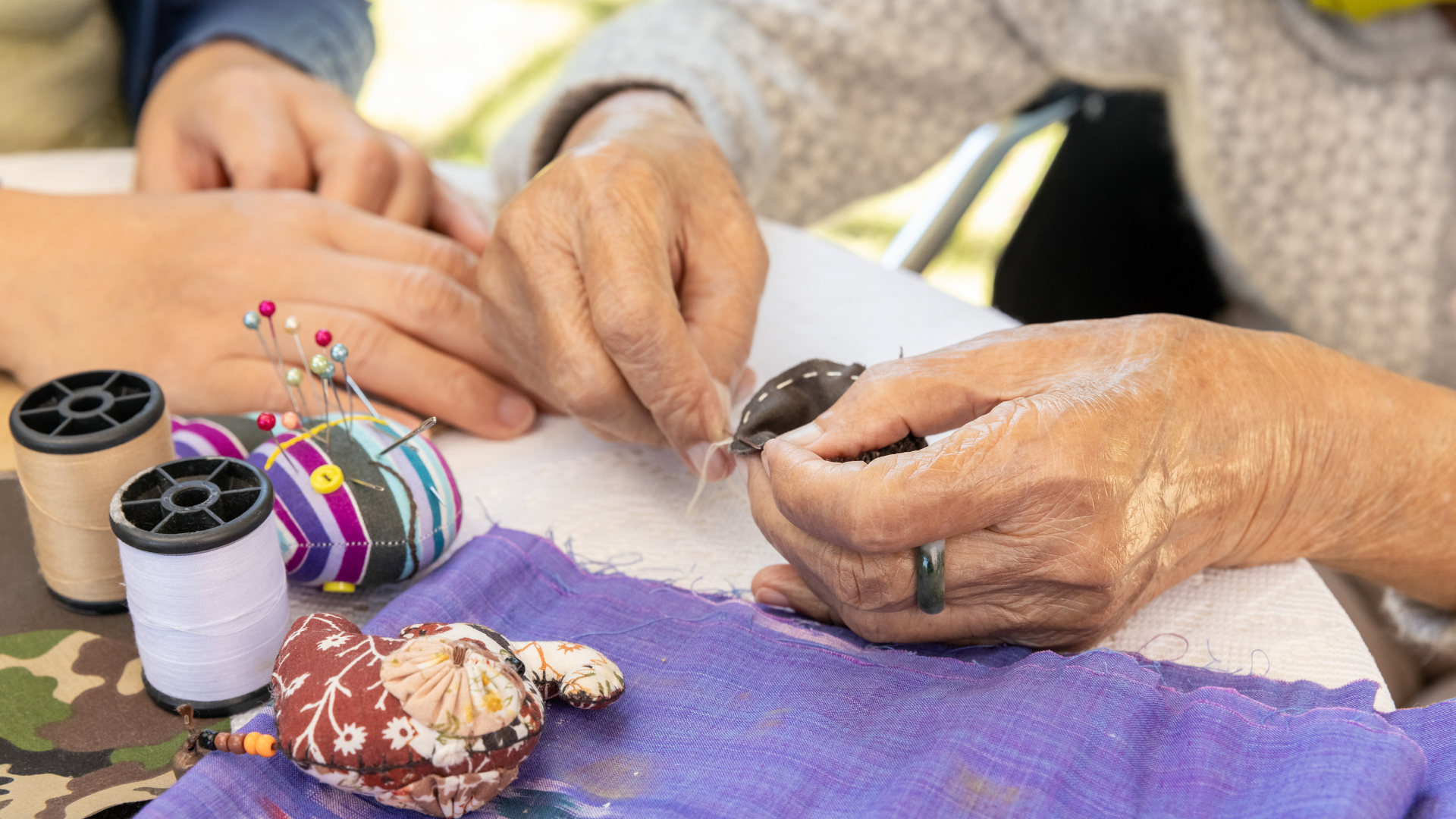 Hands sewing with thread, next to spools of thread and a pincushion.