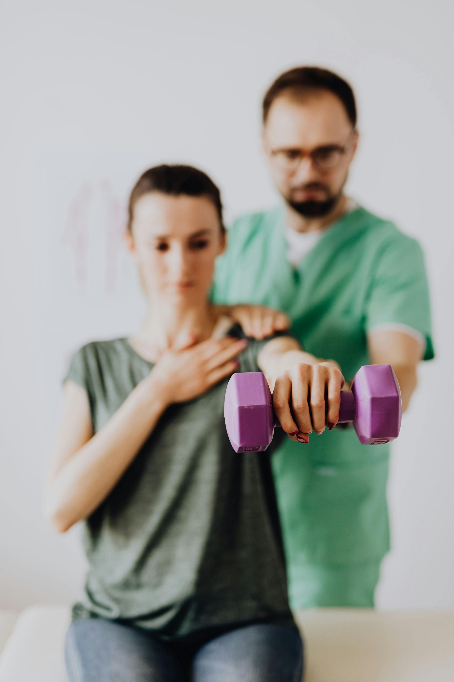 Woman using purple dumbbell for exercise, assisted by a healthcare professional in green scrubs.