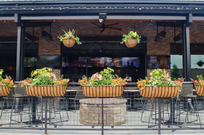 Interior of a crowded sports bar with tables, bar seating, TV screens, and servers carrying food.