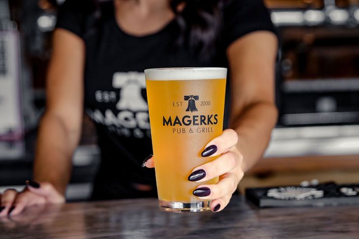 Bartender holding a pint of beer at Magerk's Pub & Grill. The beer is golden, the bartender is wearing a black shirt.