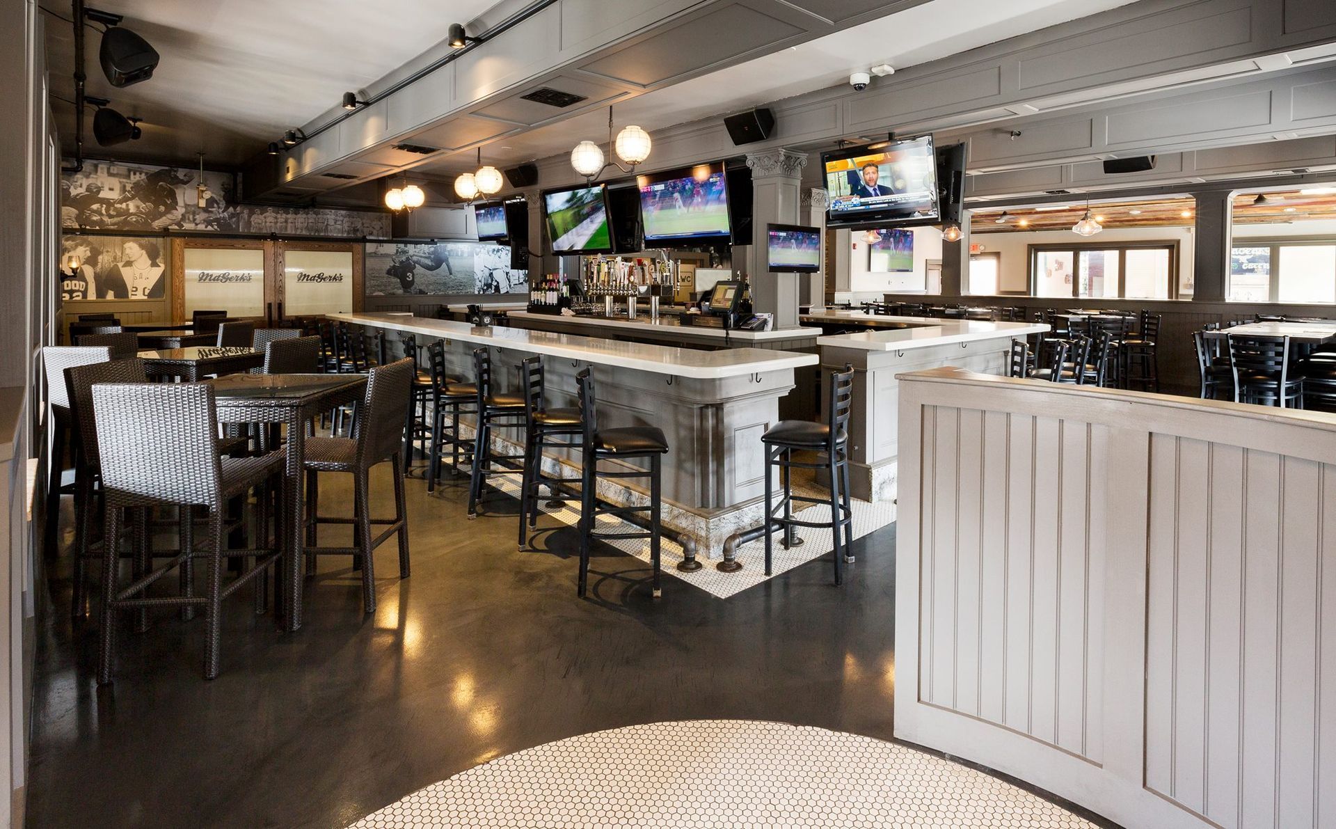 Interior of a crowded sports bar with tables, bar seating, TV screens, and servers carrying food.