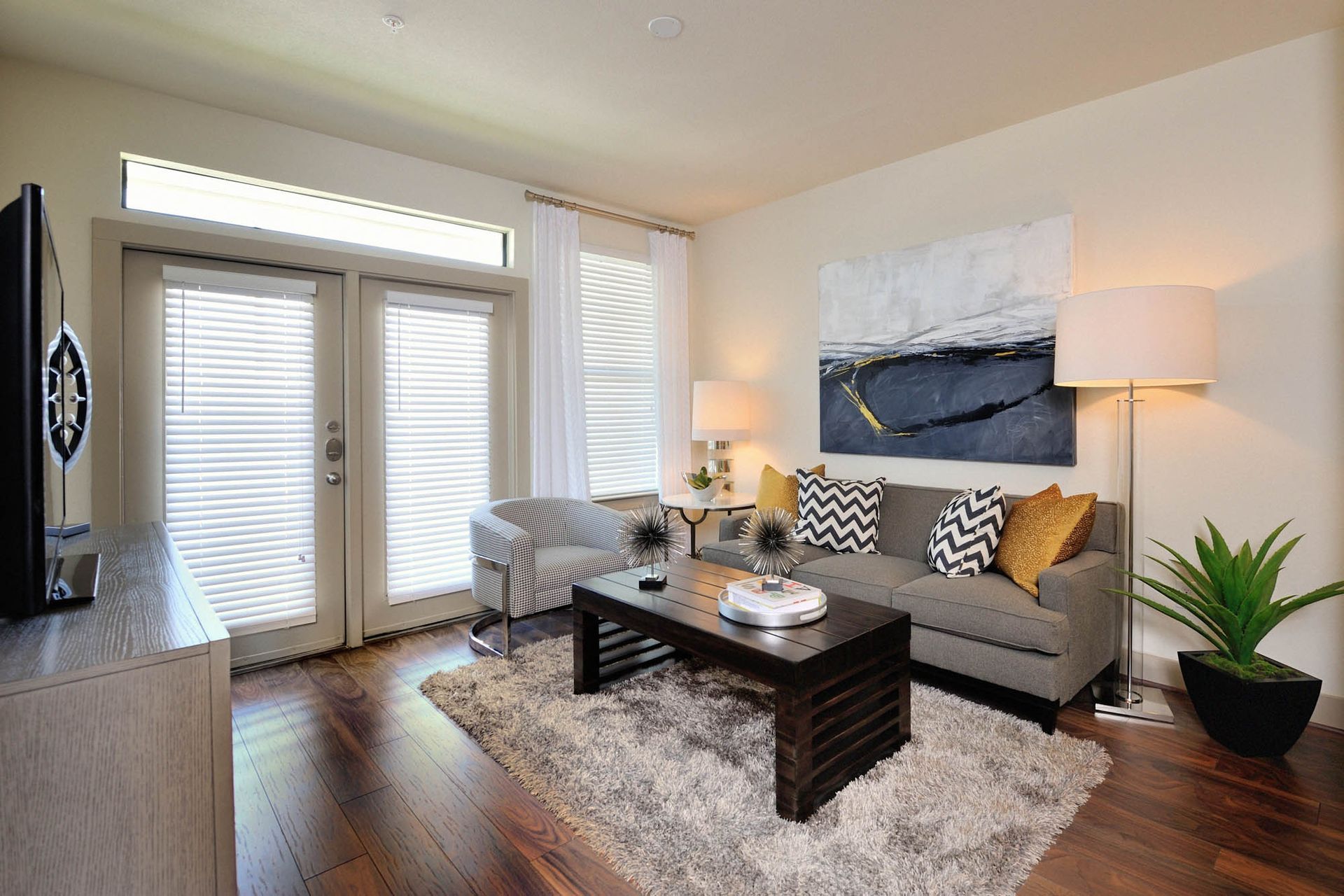 Living room in an apartment with sofa, chairs, coffee table, rug, and plants.