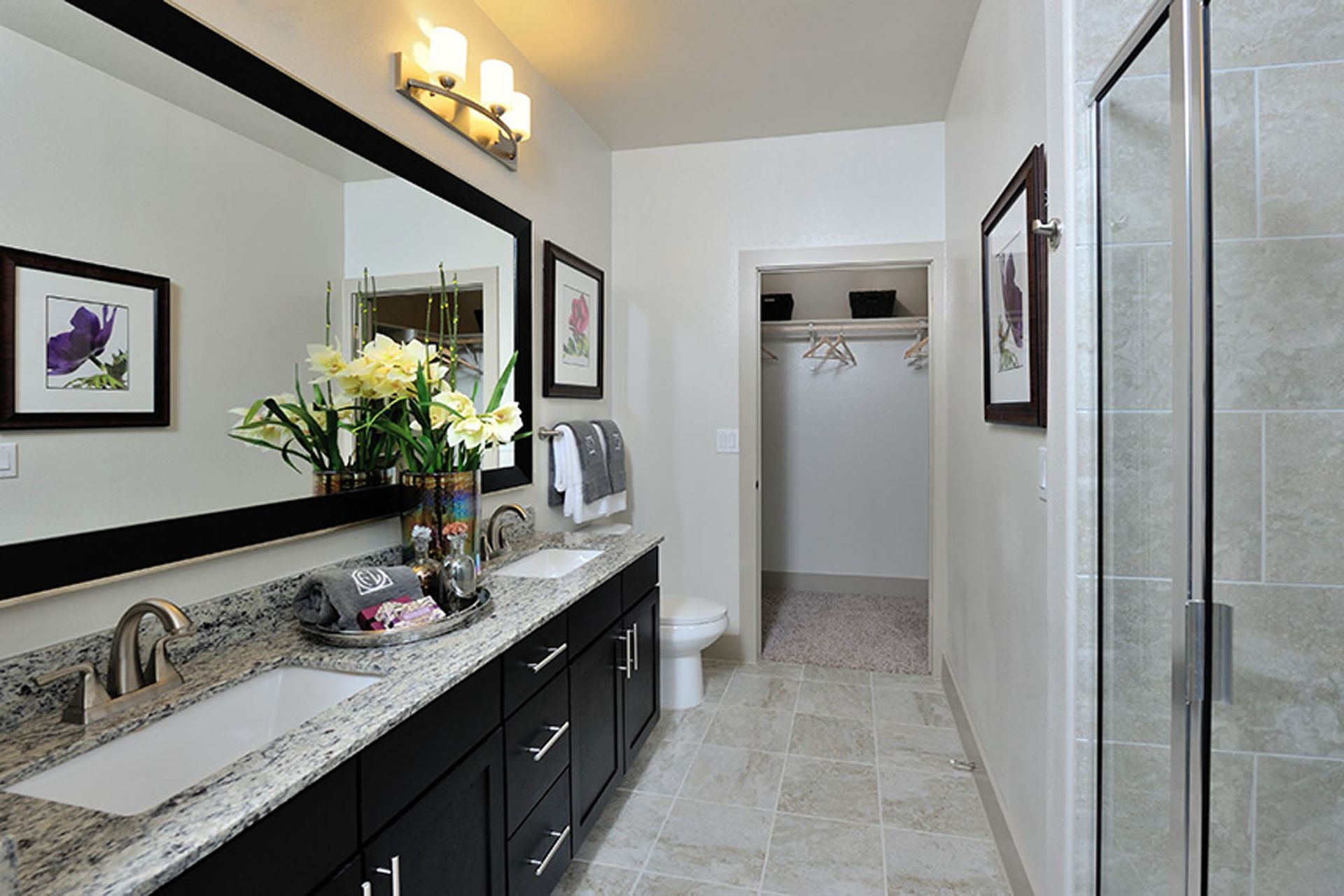 Modern apartment bathroom with double vanity, granite countertop, and glass shower.