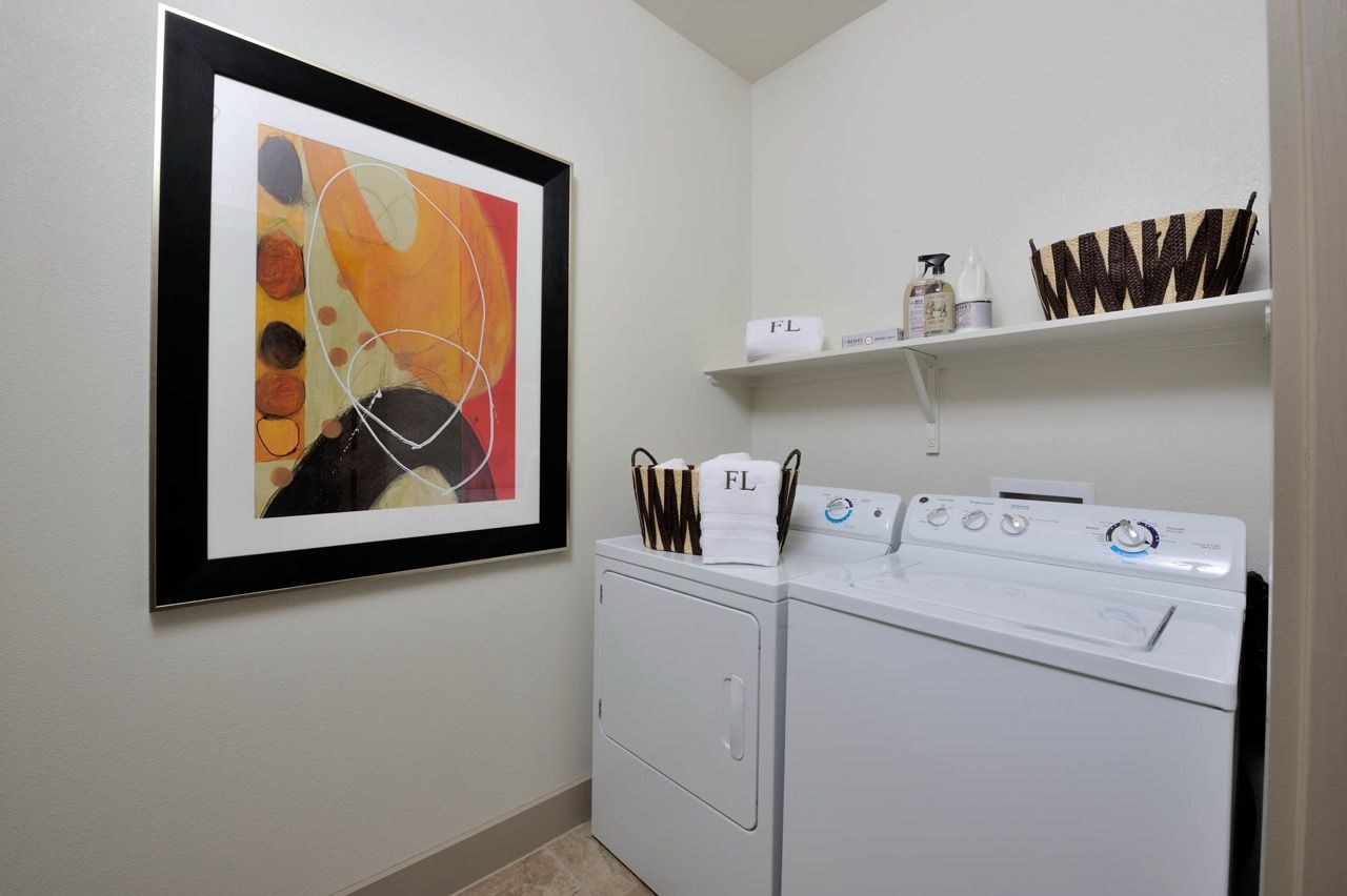 Laundry room with a front-loading dryer, a top-loading washer, shelves, and framed wall art.