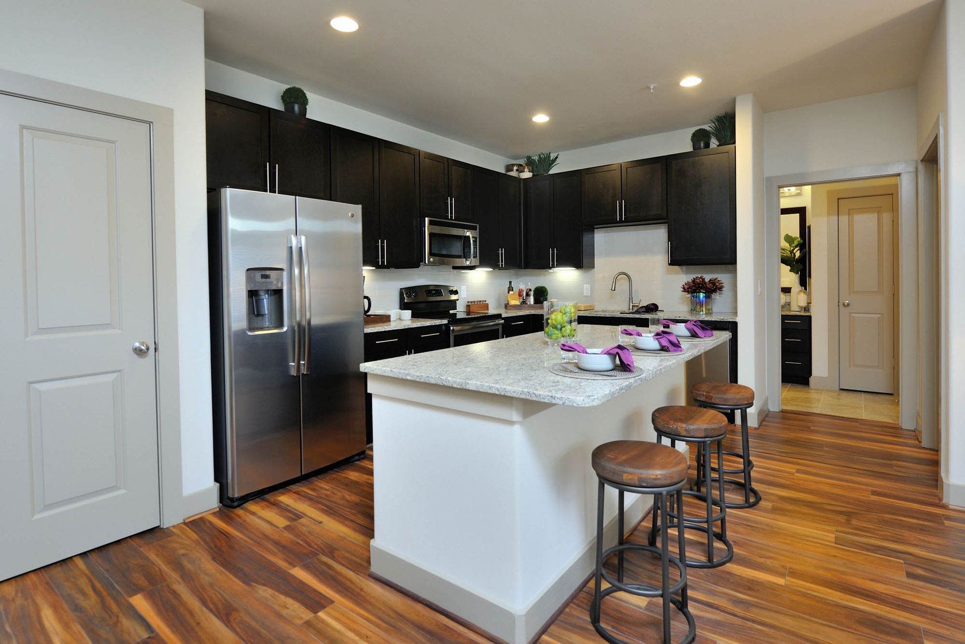 Open-concept kitchen with granite island, stainless-steel appliances, and dark wood cabinets.