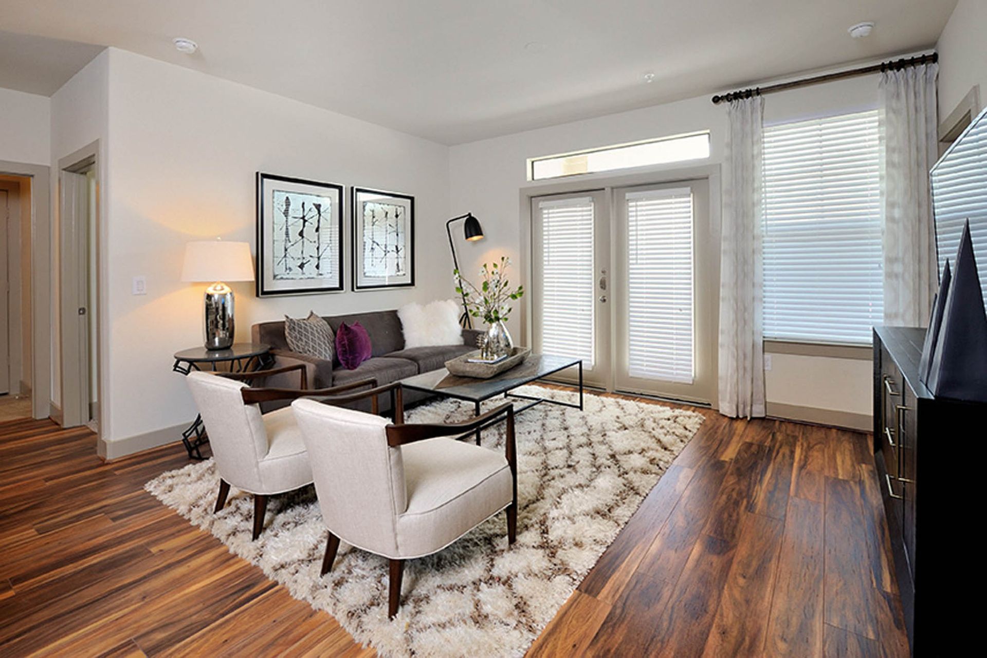 Living room in a modern apartment with hardwood floors, a sofa, chairs, and window blinds.