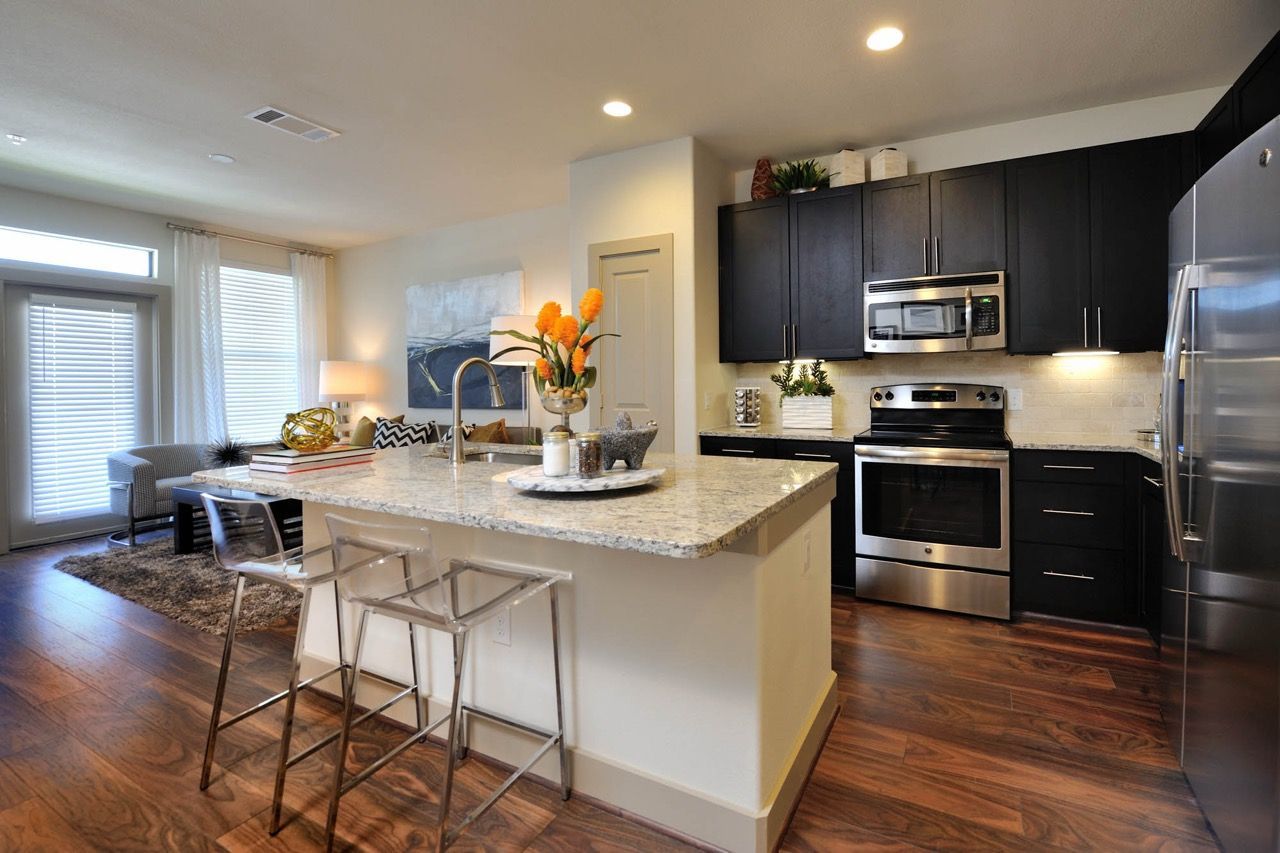 Open-concept kitchen with marble island, stainless-steel appliances, dark cabinets, and hardwood floors.