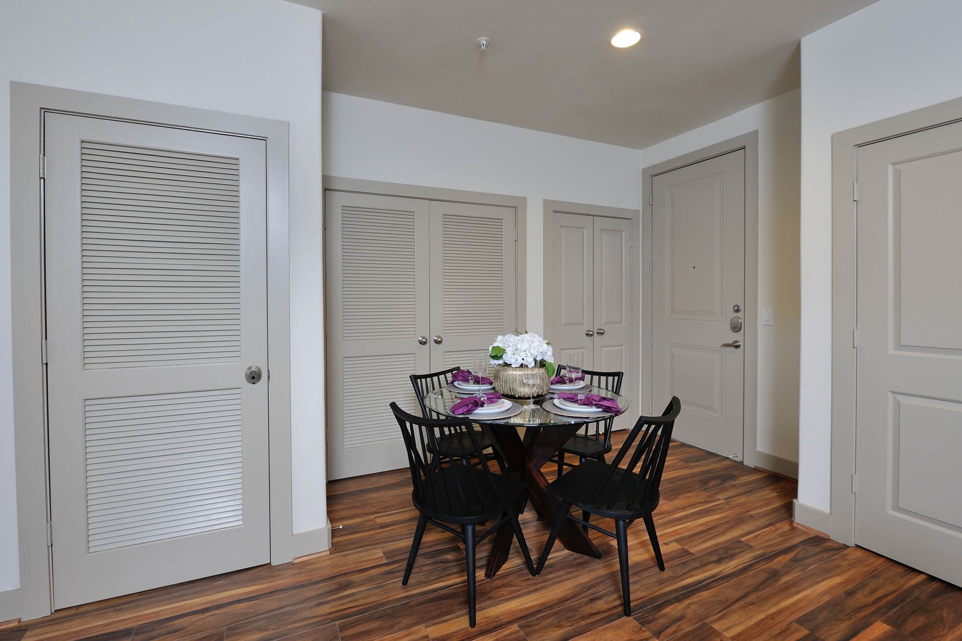 Neutral apartment dining area with round glass table, black chairs, and multiple closet doors.