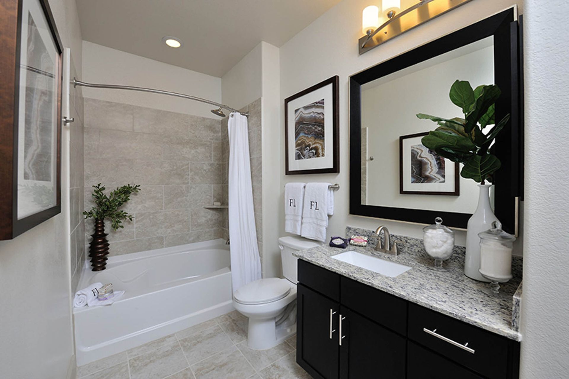 Bathroom with granite countertop, dark vanity, large framed mirror, and shower-tub with beige tile.