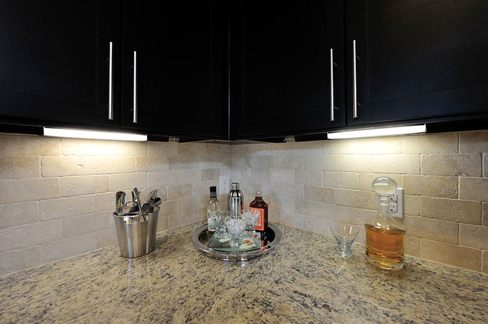 Kitchen with granite countertop, dark cabinets, under-cabinet lights, and barware on the counter.