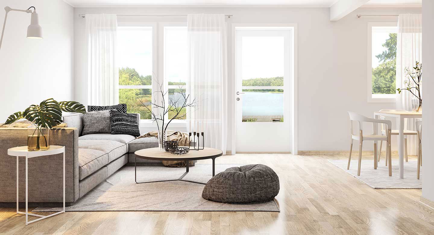 A bright, minimalist living room with a light gray sectional, wooden coffee table, and a small dining area.