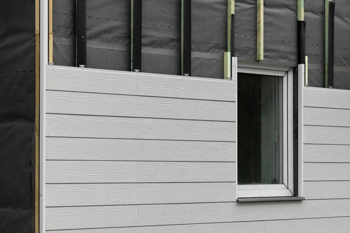 Light gray horizontal wood-look siding installed over a black weather-resistant barrier around a white-framed window.