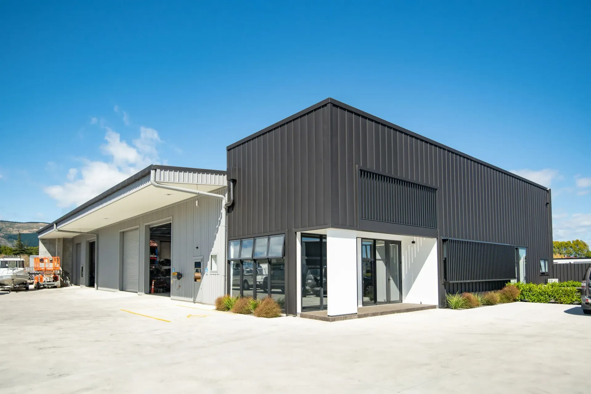 Modern commercial building with a black corrugated facade and a white entryway, next to a warehouse with an overhang.