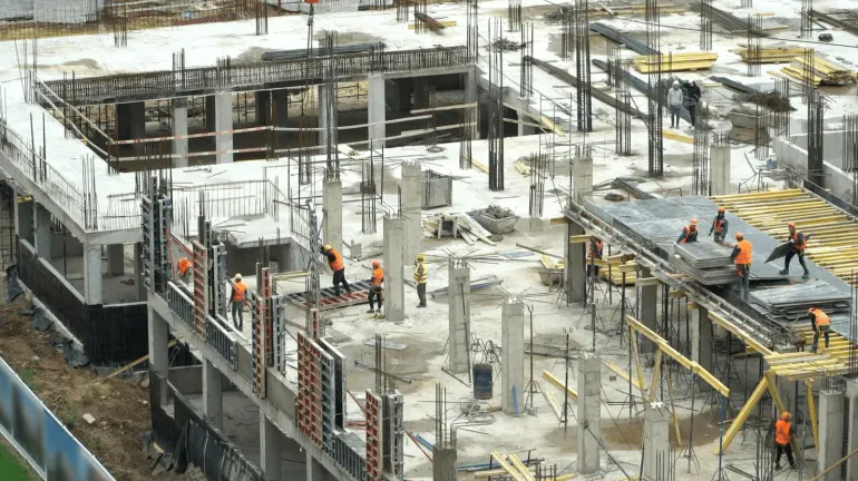 High-angle view of a construction site with workers in safety vests installing rebar and forms on a concrete frame.