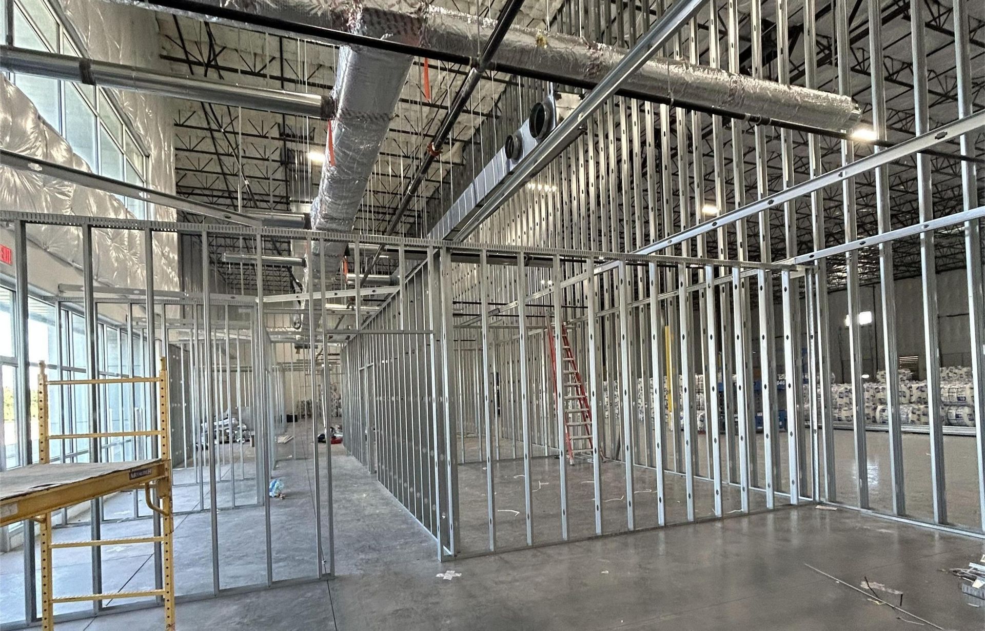 An interior view of a commercial space under construction with metal wall framing and exposed ceiling ducts.