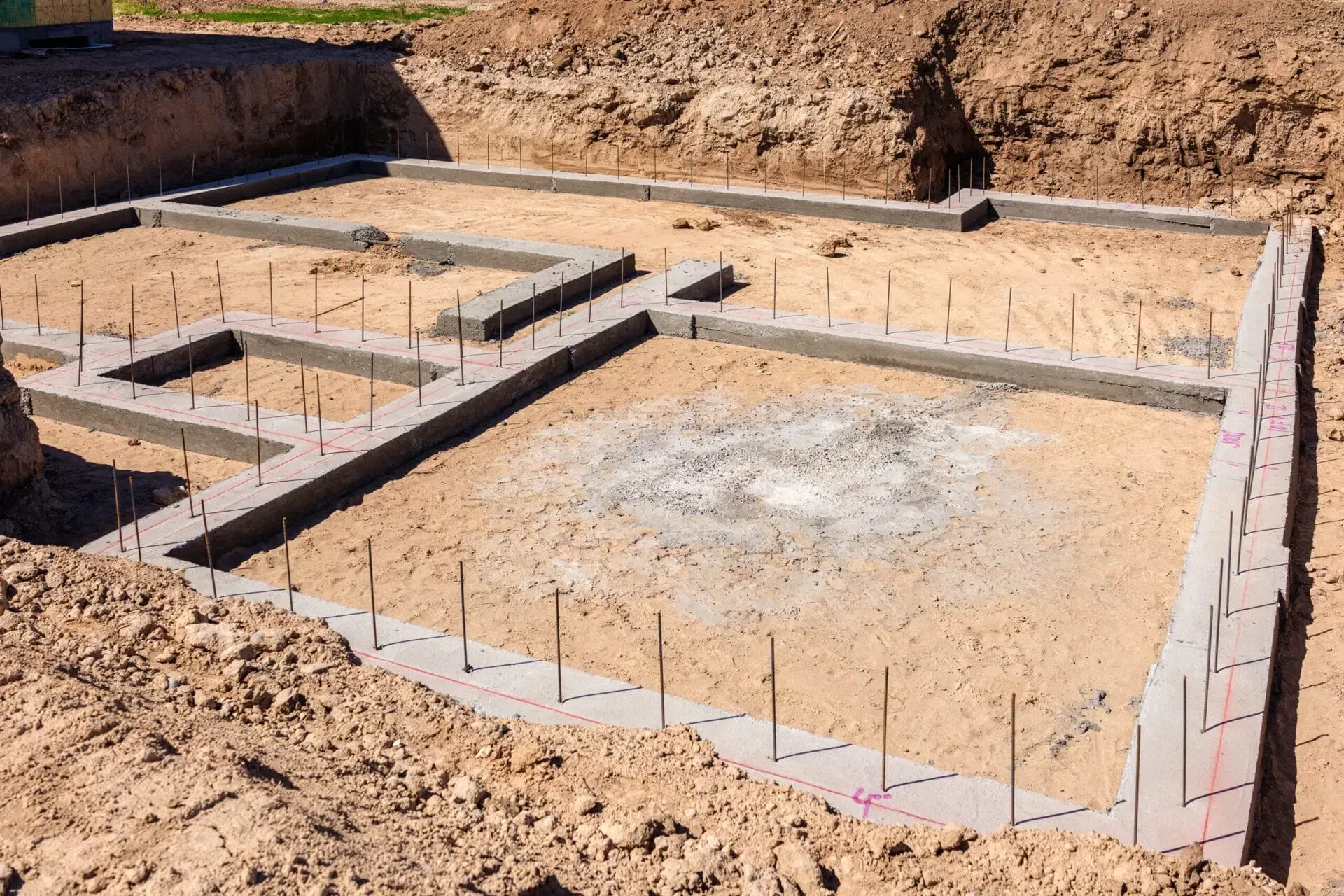 Concrete building foundation with upright rebar studs in a dirt excavation site.