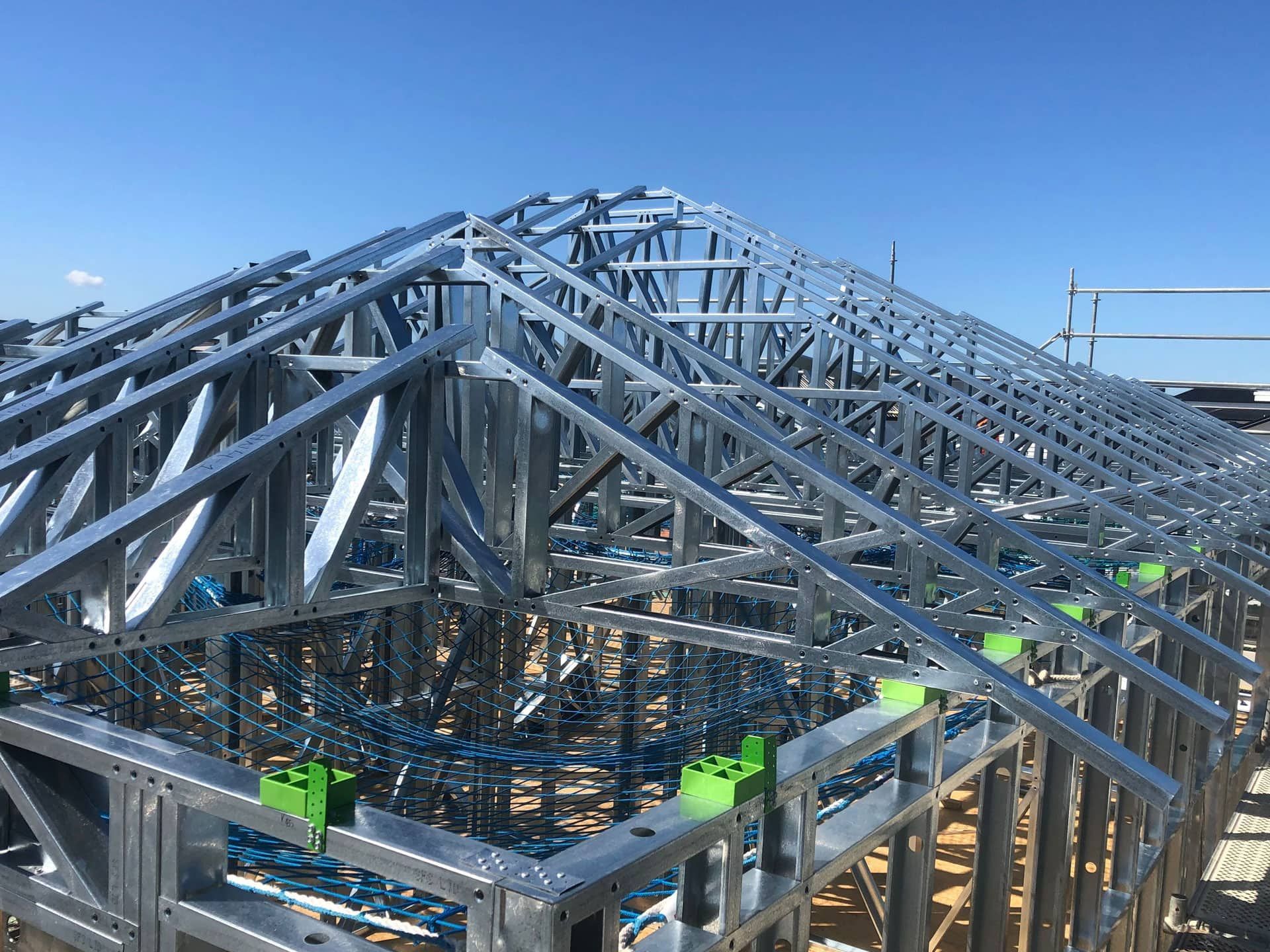A steel truss framework of a house roof under construction against a clear blue sky.